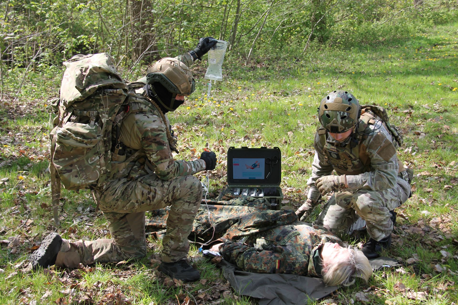 Two military operators providing TCCC guided care with ResCura Smart Medikit in outdoor field environment