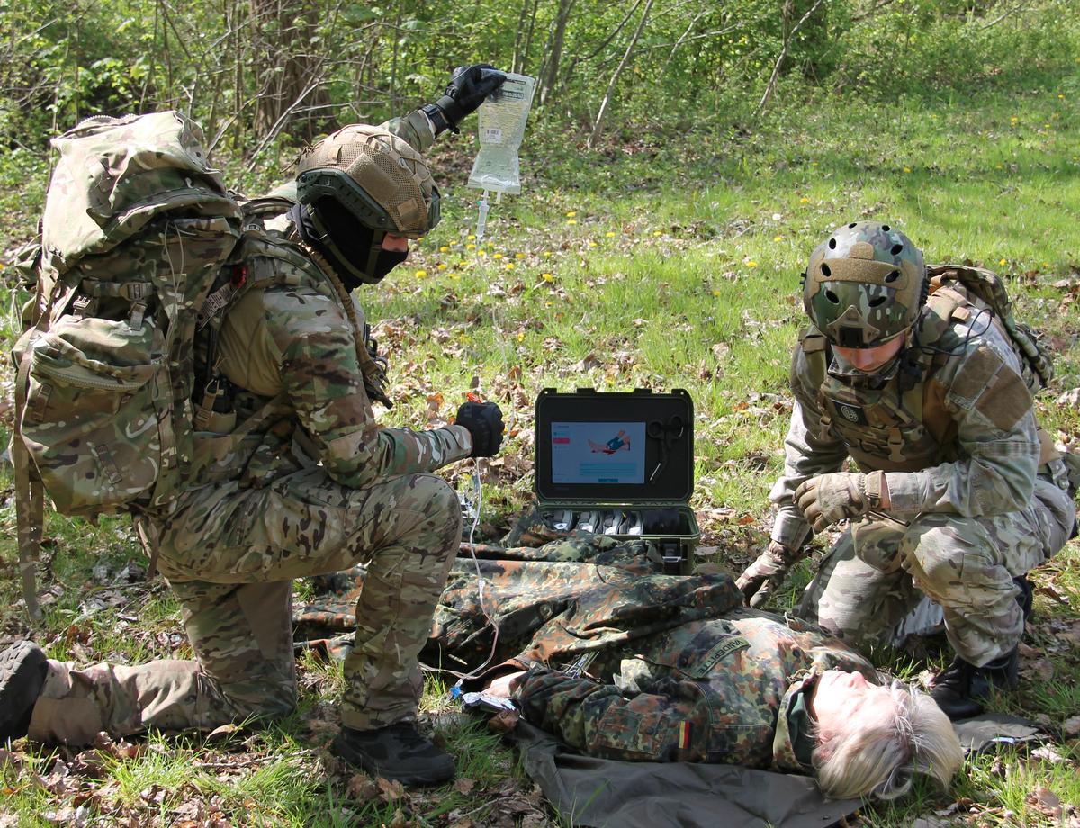 ResCura Smart Medikit open in field — integrated touchscreen showing guided TCCC protocol, military operators treating casualty